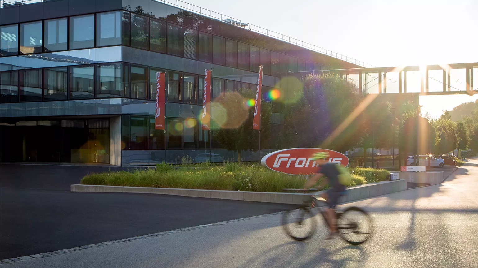 Ein Radfahrer quert im Sonnenschein die Straße vor dem Fronius Gebäude.