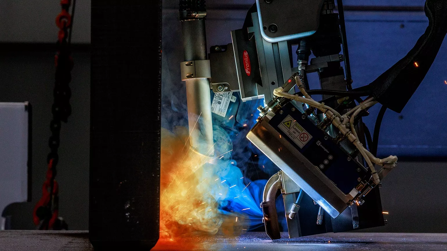 Automatisierter Schweißkopf bei einem industriellen Schweißprozess mit Funkenflug und Rauch in einer Fertigungsumgebung.