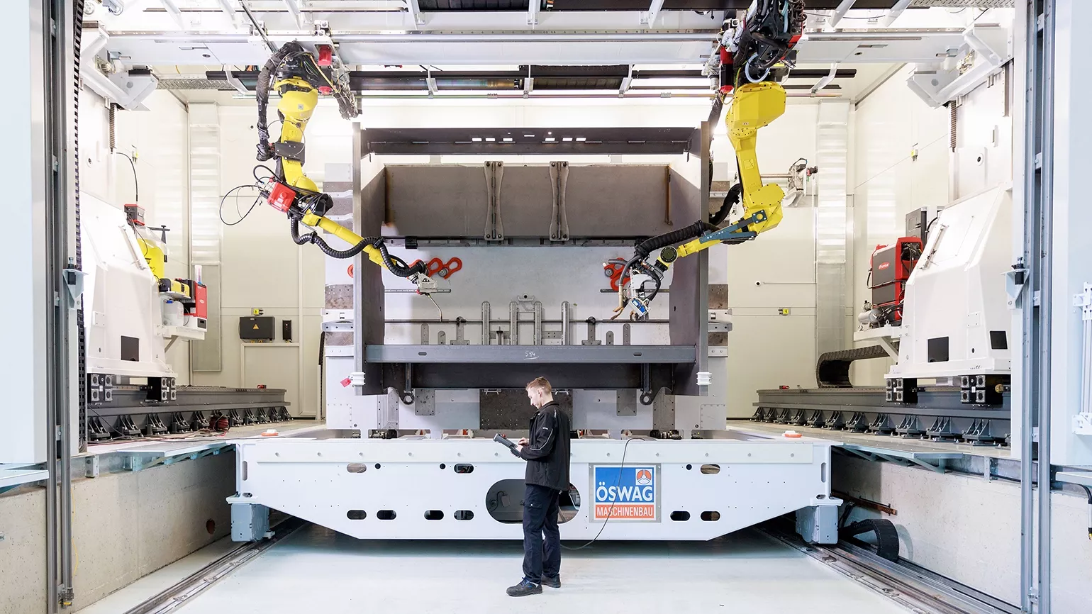 Großformatige automatisierte Fertigungsanlage mit Industrierobotern und Bedienperson in einer modernen Produktionshalle.