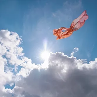 A piece of pink, translucent fabric floating in the sky against bright sunlight and white clouds.