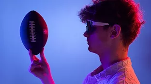 Ein junger Mann hält einen Football in der Hand, blauer Hintergrund.