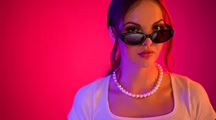 Junge Frau mit schwarzer Sonnenbrille vor pinkem Hintergrund