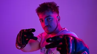 Junger Mann mit Handschuhen vor lila Hintergrund.