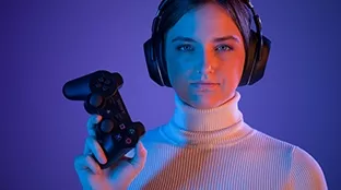 Junge Frau mit Kopfhörern und einem Controller in der Hand, blauer Hintergrund.