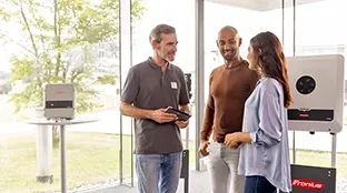 Three people standing in a modern room discussing Fronius solar technology products.