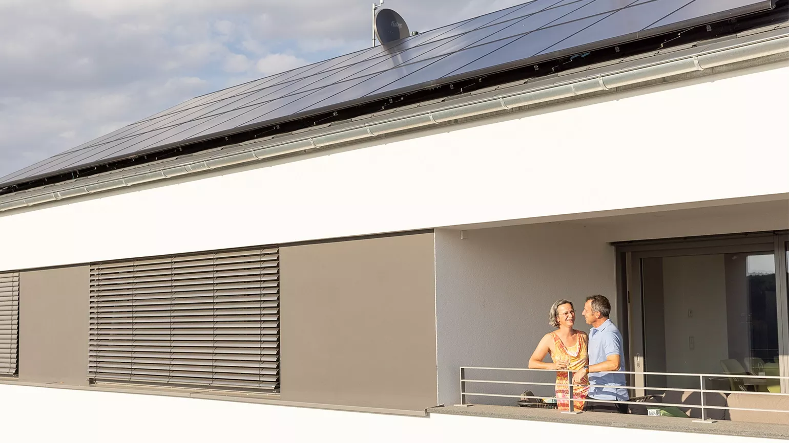 Ein Ehepaar steht am Balkon, ihre Solar Panele sind zu sehen, die Energie in den Fronius Wechselrichter übergeben.