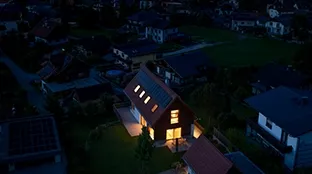 Hell erleuchtetes Haus dank Fronius Gesamtlösung, umgeben von dunklen Häusern ohne Strom.