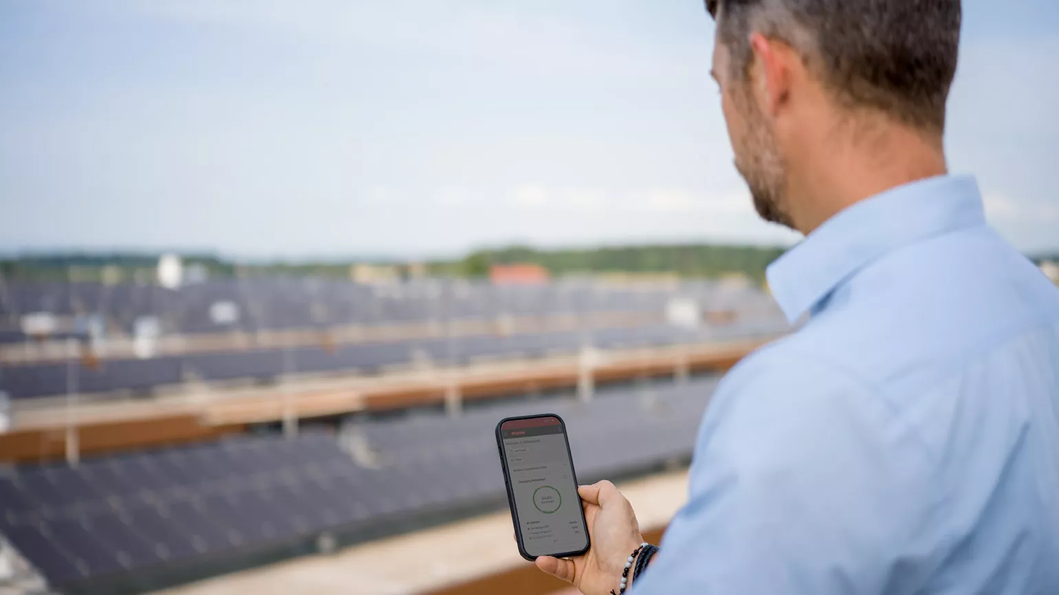man with mobile phone, using Charge & Connect app, on a roof with solar panels